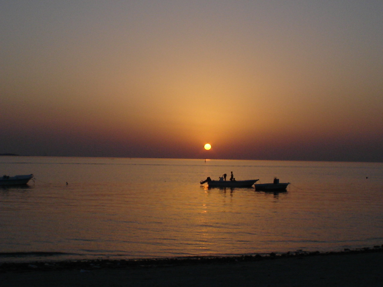 Small boats silhouetted at sunset off Budaiya Beach in Bahrain